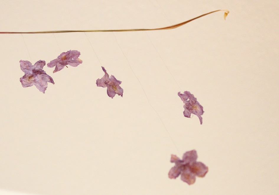 Foto eines Kunstwerkes mit fünf Blüten, aufgehängt mit Haaren an einem Yucca-Palmblatt